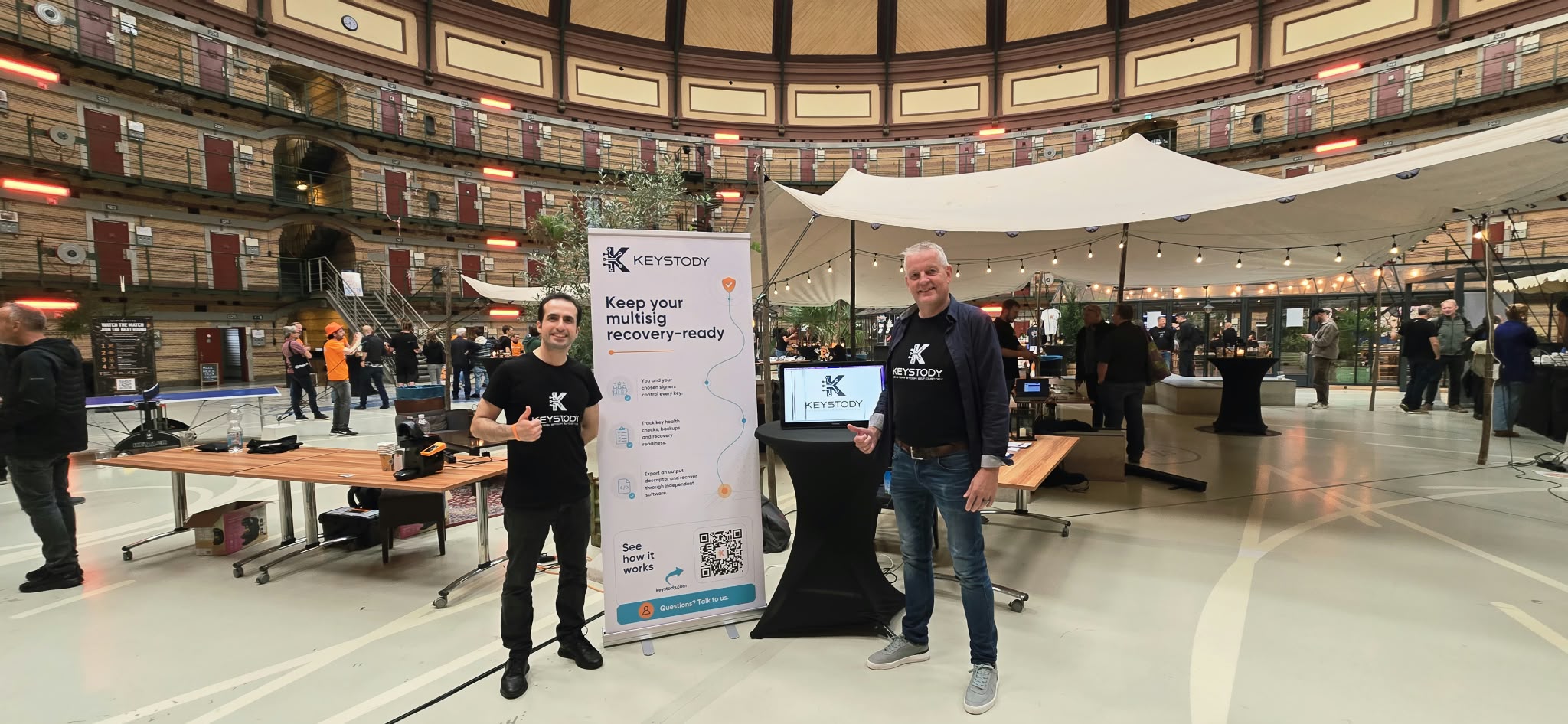 The Keystody booth under the dome of the Koepelgevangenis: the banner, a demo screen on a high table, and two people in Keystody shirts