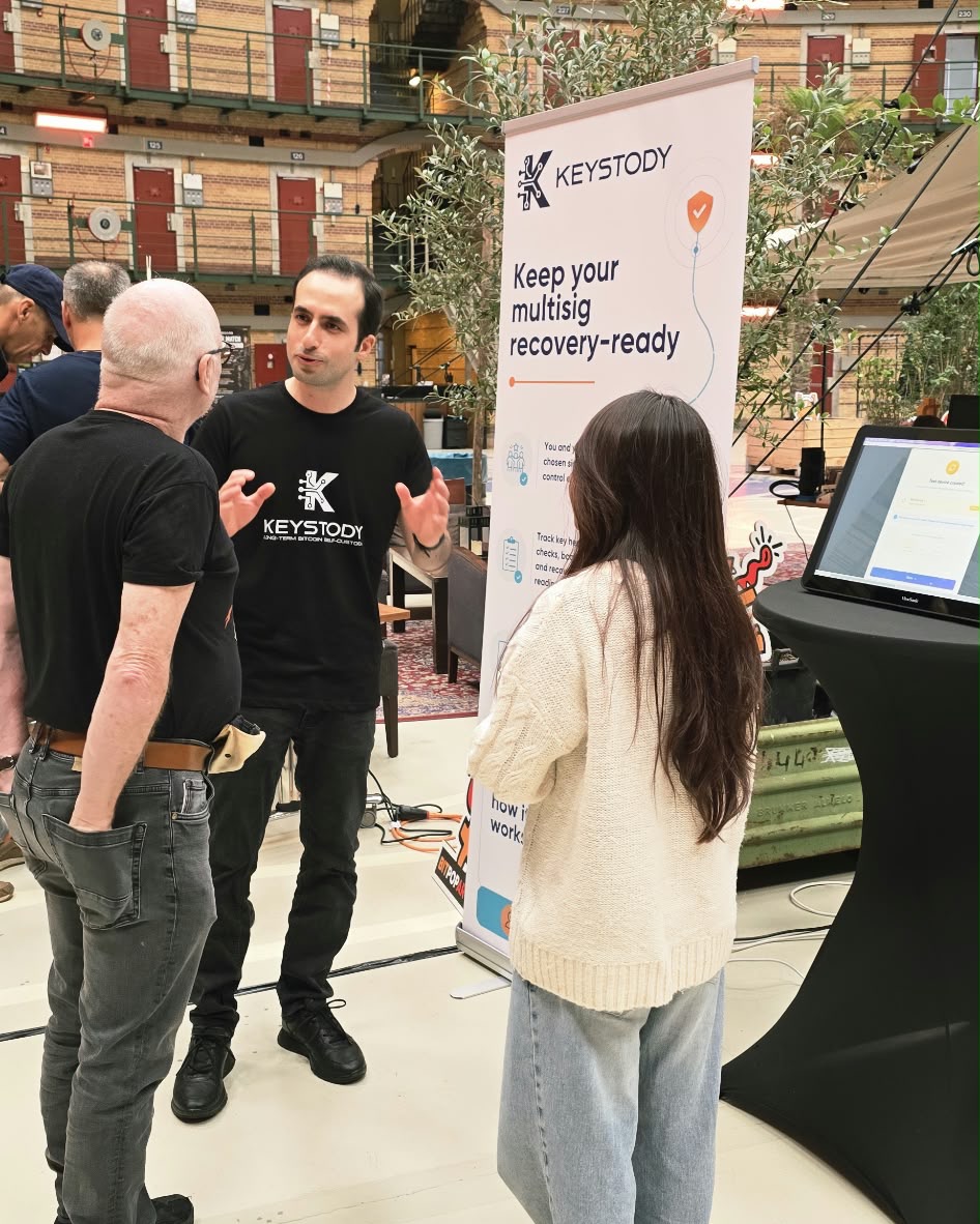 Explaining 2-of-3 multisig to two visitors at the booth, under the galleries of the Koepelgevangenis