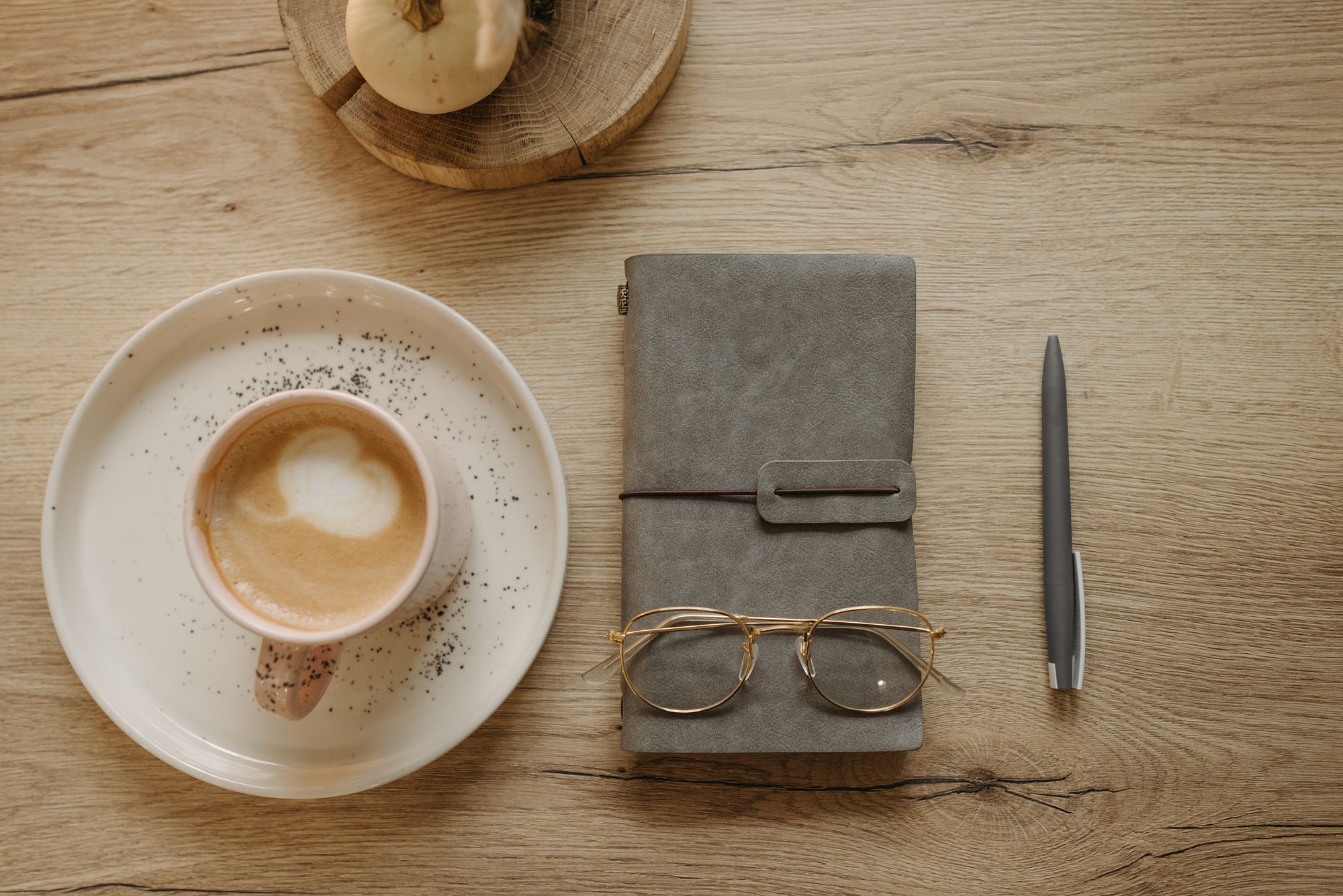 A notebook, a pen, reading glasses and a coffee on an oak table