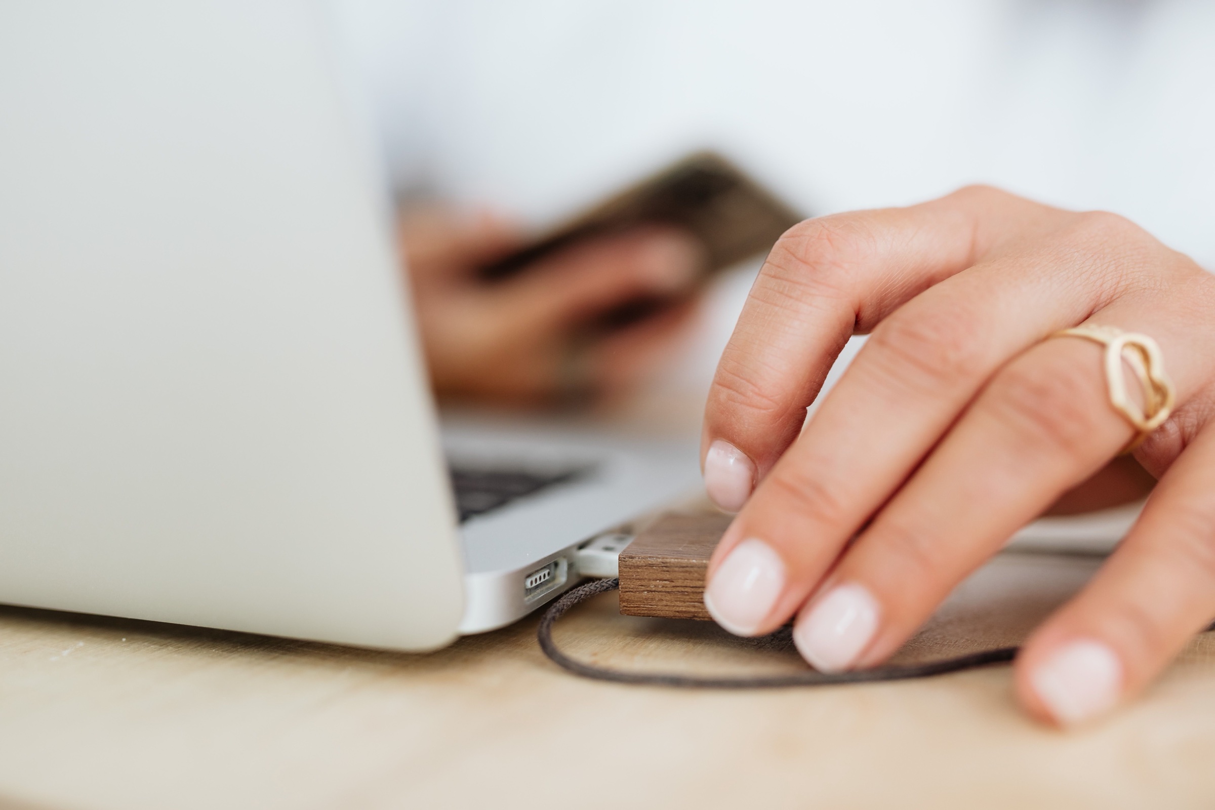 A hand connecting a small device to a laptop on a light wooden desk